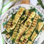 Grilled zucchini slices topped with mint leaves on round plate.
