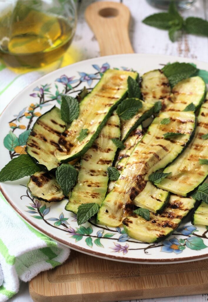 Plated grilled zucchini with mint and olive oil bottle in background.