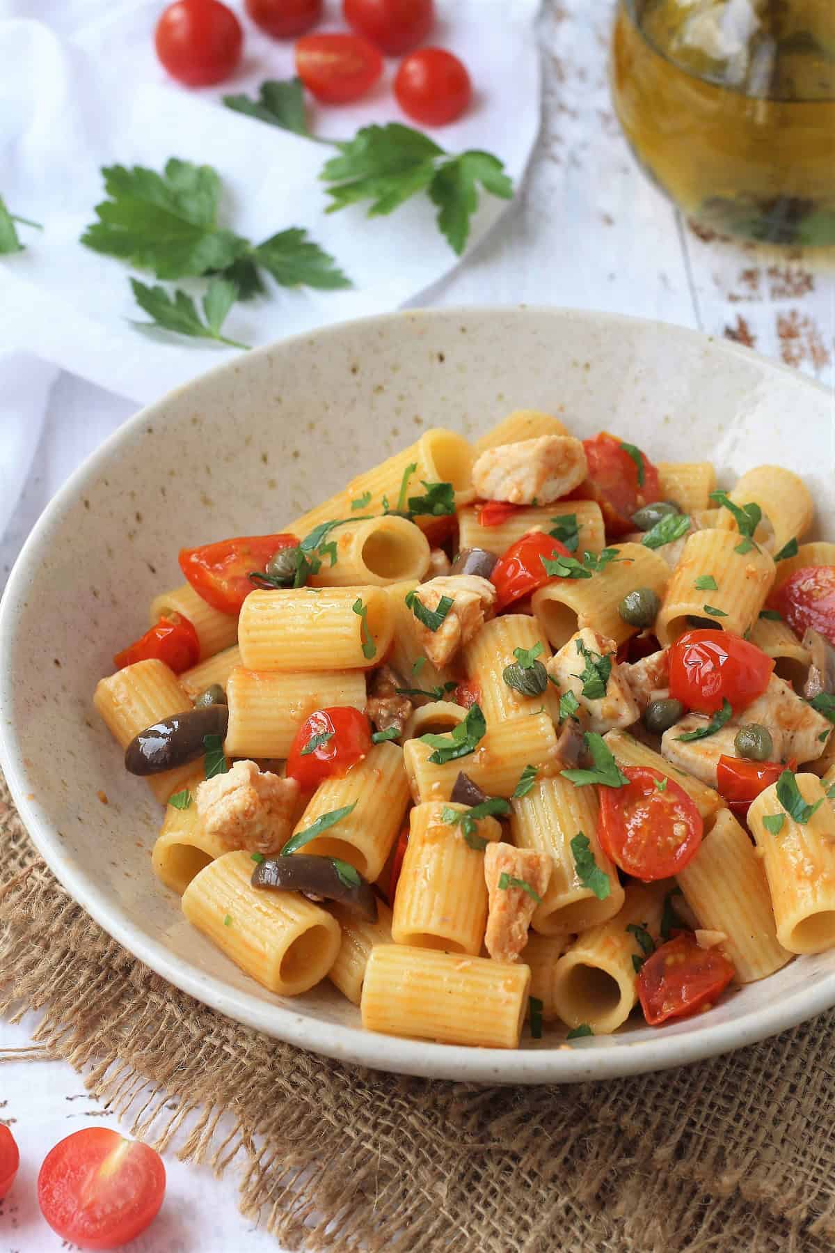Swordfish pasta with cherry tomato sauce in bowl surrounded by cherry tomatoes, fresh parsley and olive oil bottle.