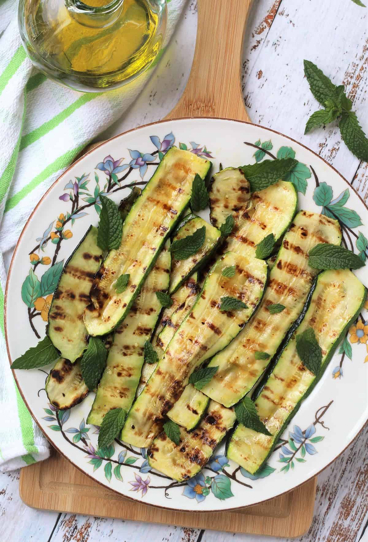 Grilled zucchini with mint and vinegar on round plate topped with fresh mint leaves.