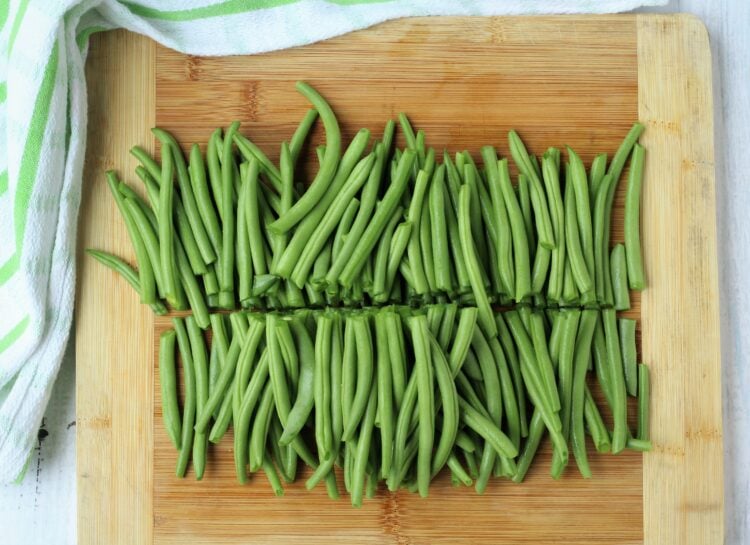Halved green beans on wood board.