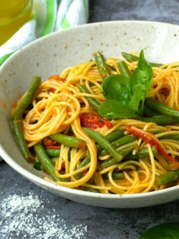 Pasta with green beans and tomato sauce in bowl topped with basil.