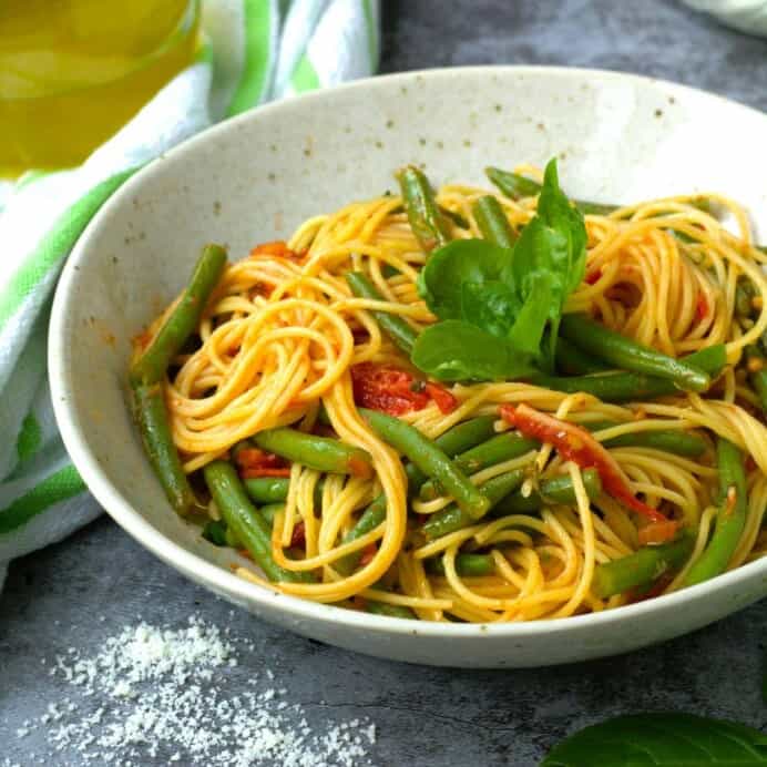 Pasta with green beans and tomato sauce in bowl topped with basil.