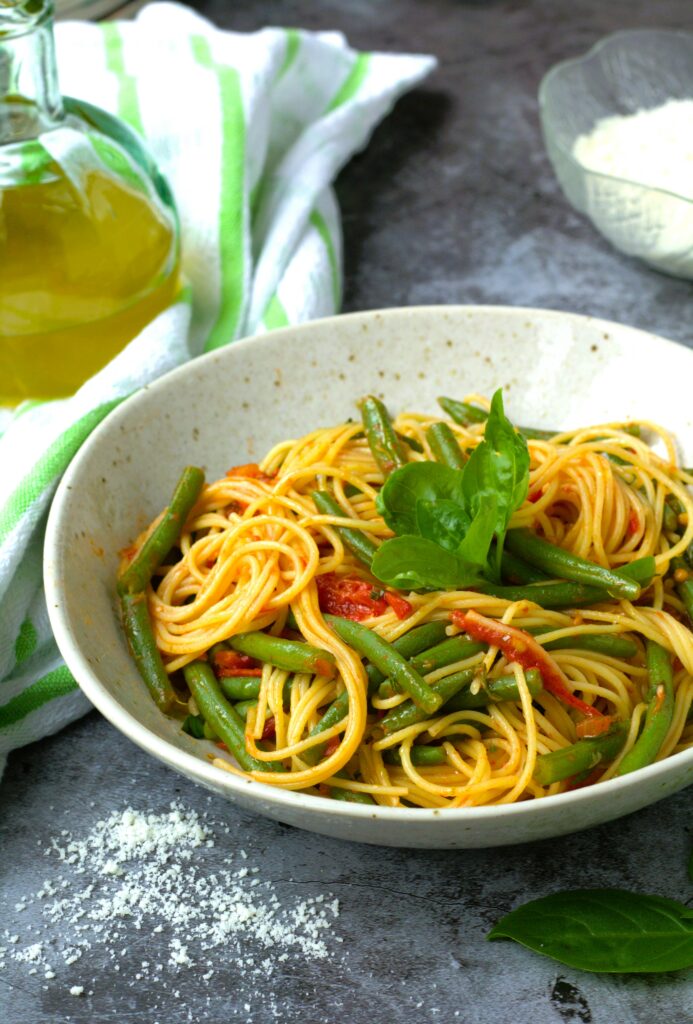 Green beans with tomato sauce and pasta in bowl topped with basil.