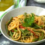 Spaghetti with green beans in tomato sauce with basil in bowl.