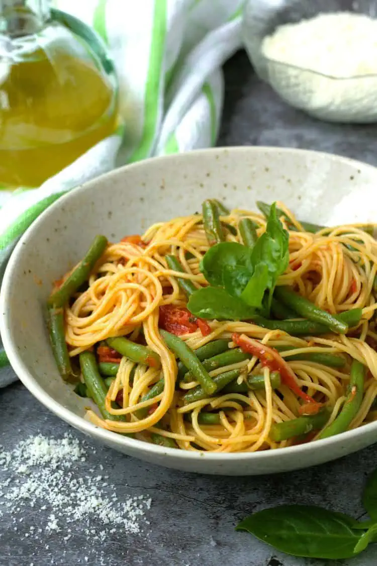 Spaghetti with green beans in tomato sauce with basil in bowl.