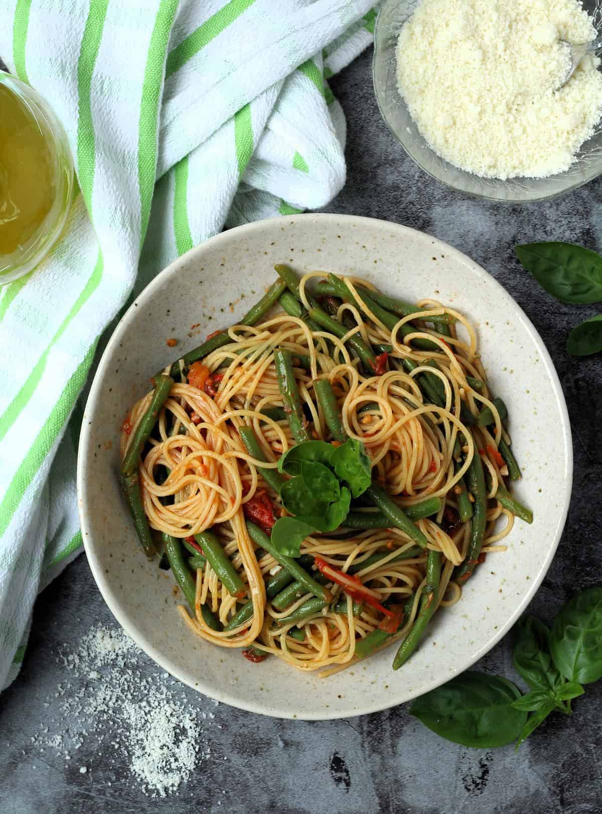 Pasta with green beans and tomato sauce in bowl next to bowl of grated cheese.
