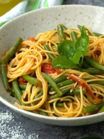 Pasta with green beans and tomato sauce in bowl topped with basil.