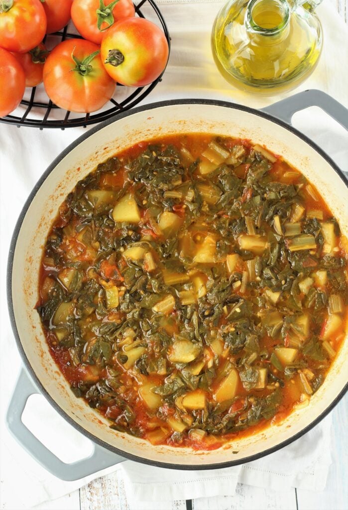 Swiss chard braised in skillet with tomatoes and potatoes.