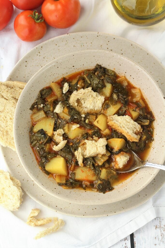 Bowl of swiss chard with potatoes and tomatoes and bread in it.