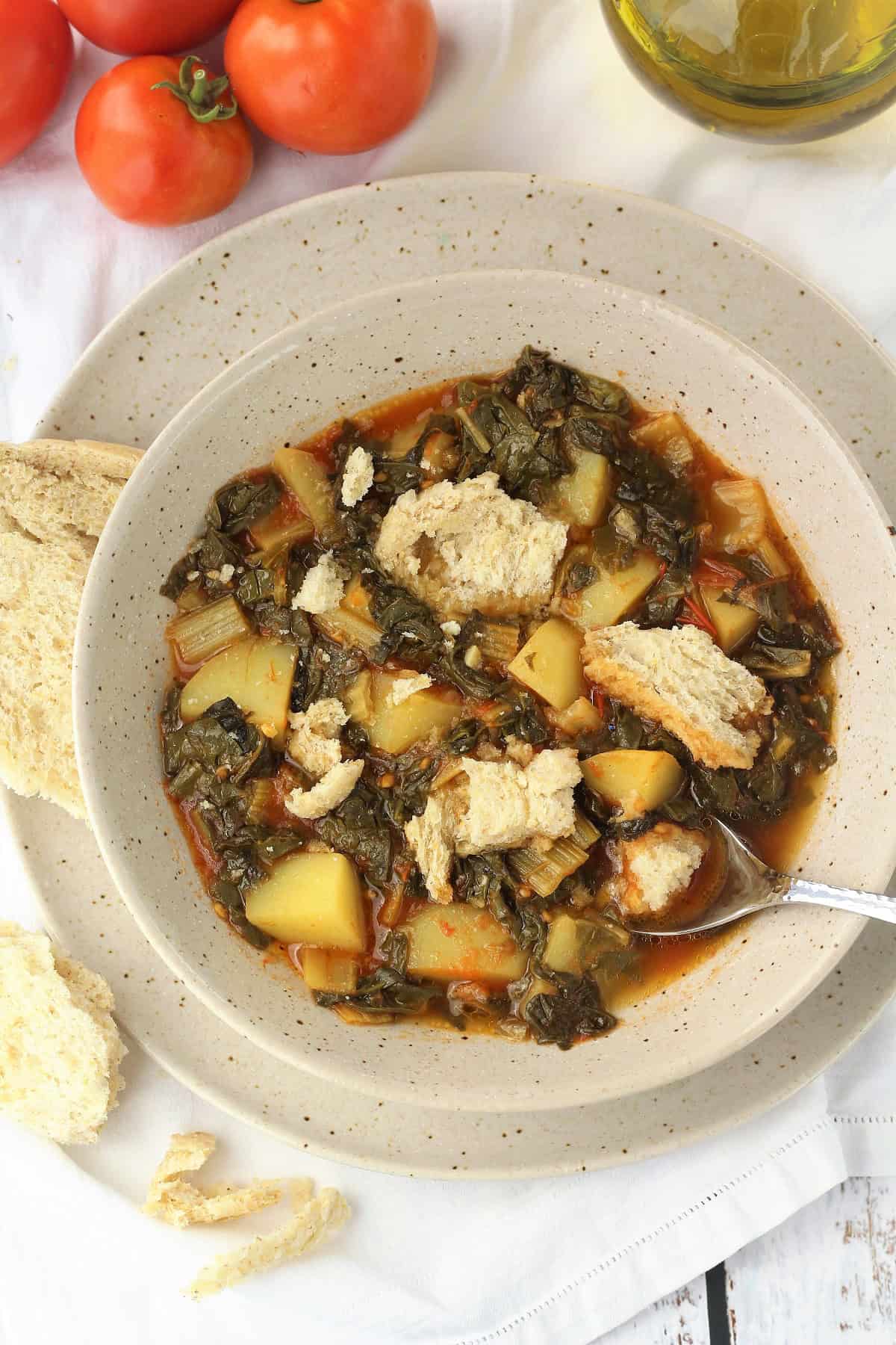 Stewed swiss chard with potatoes served with hunks of bread in bowl.