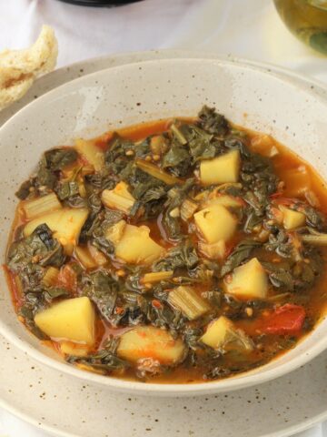 Bowl of swiss chard with potatoes and tomatoes with bread on side.