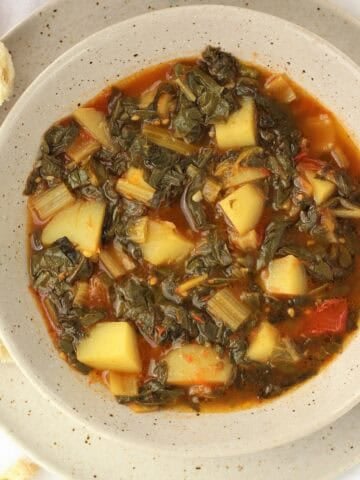 Stewed swiss chard recipe with potatoes and tomatoes in bowl with bread slices next to it.