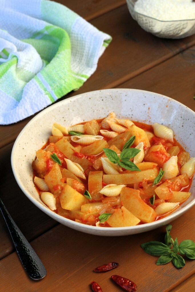 Cucuzza with pasta in bowl with basil and bowl of cheese behind it.