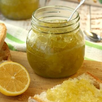 Zuccata jam in jar with slice of bread topped with jam and lemon half on wood board.