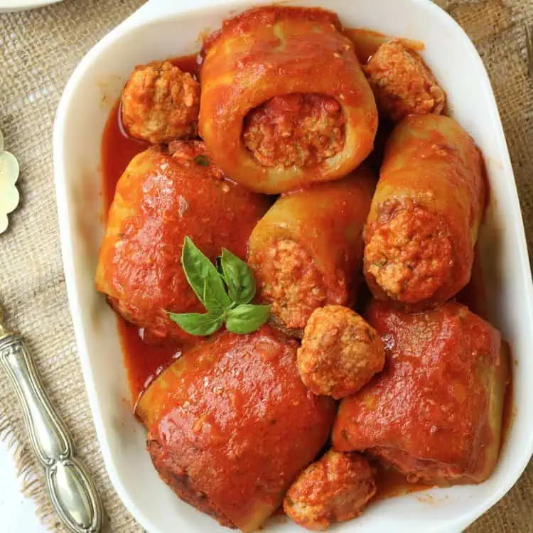 Stuffed cucuzza pieces in tomato sauce in rectangular serving dish.