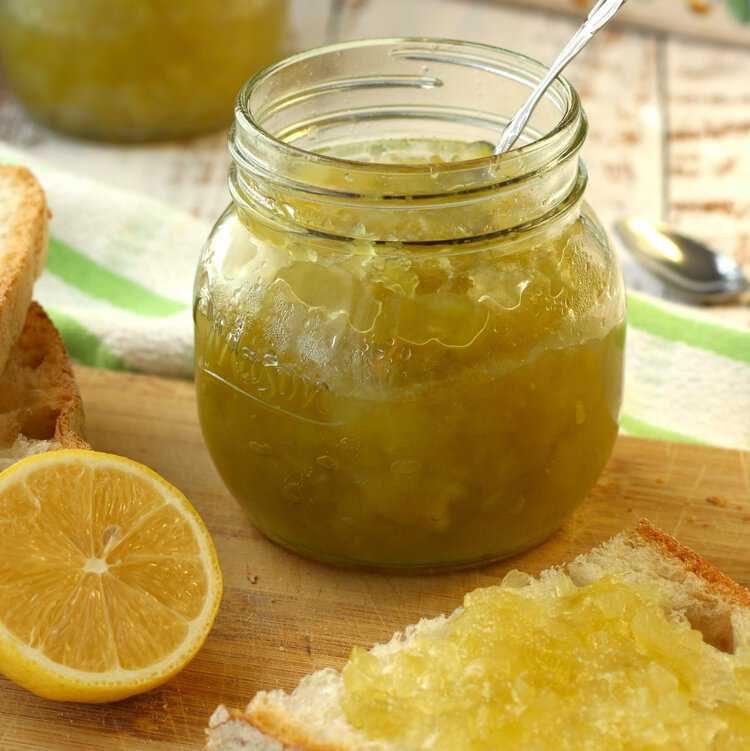 Jar of Sicilian zuccata jam on wood board next to bread and lemon half.
