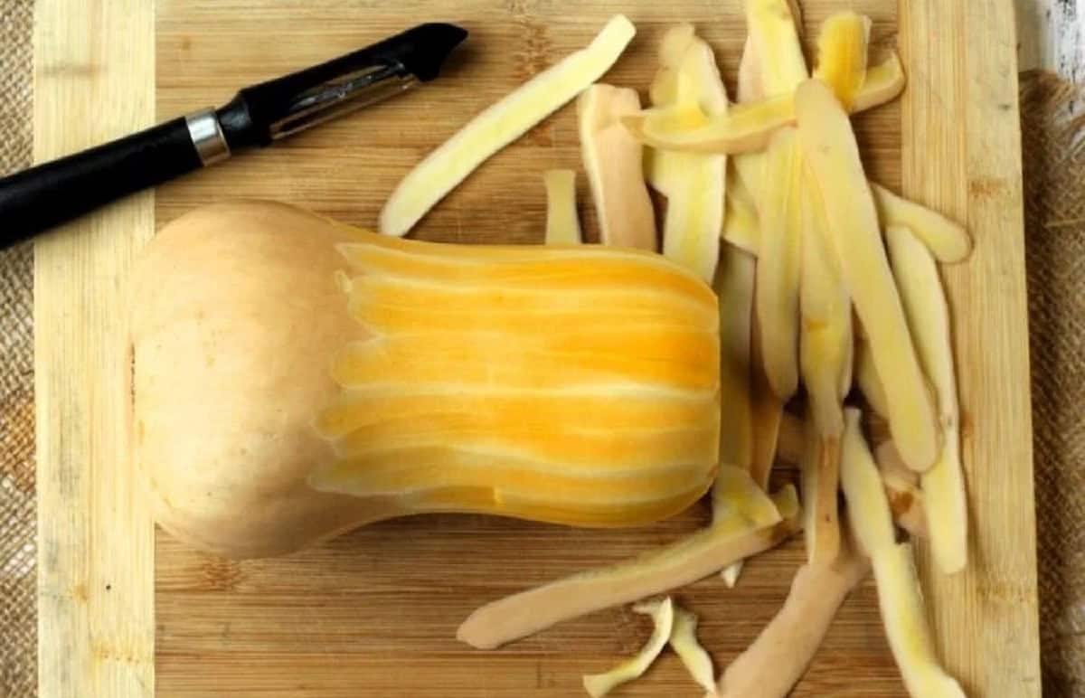 Butternut squash peeled with vegetable peeler on wood board.