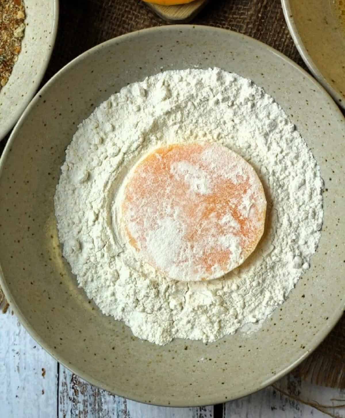 Dredged butternut squash cutlet in bowl with flour.