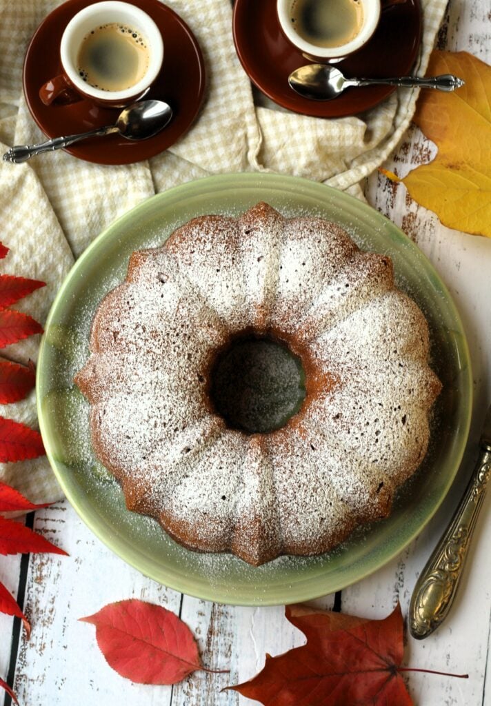 Italian Squash Cake on plate surrounded by coffee cups and leaves.