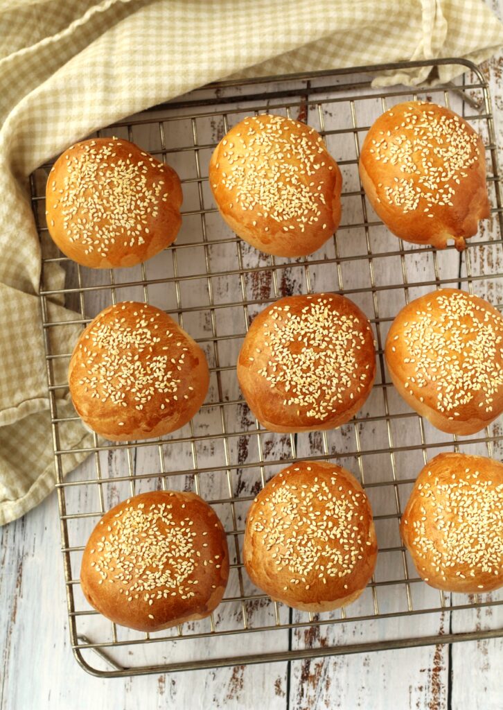 Sesame seed topped brioche buns on wire rack.