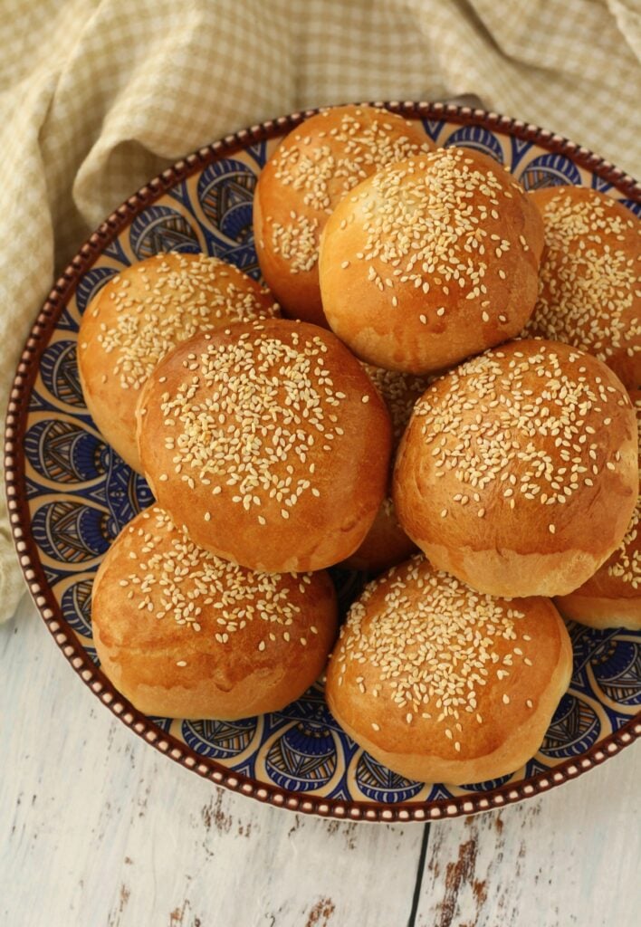 Sesame seed topped brioche buns on round plate.