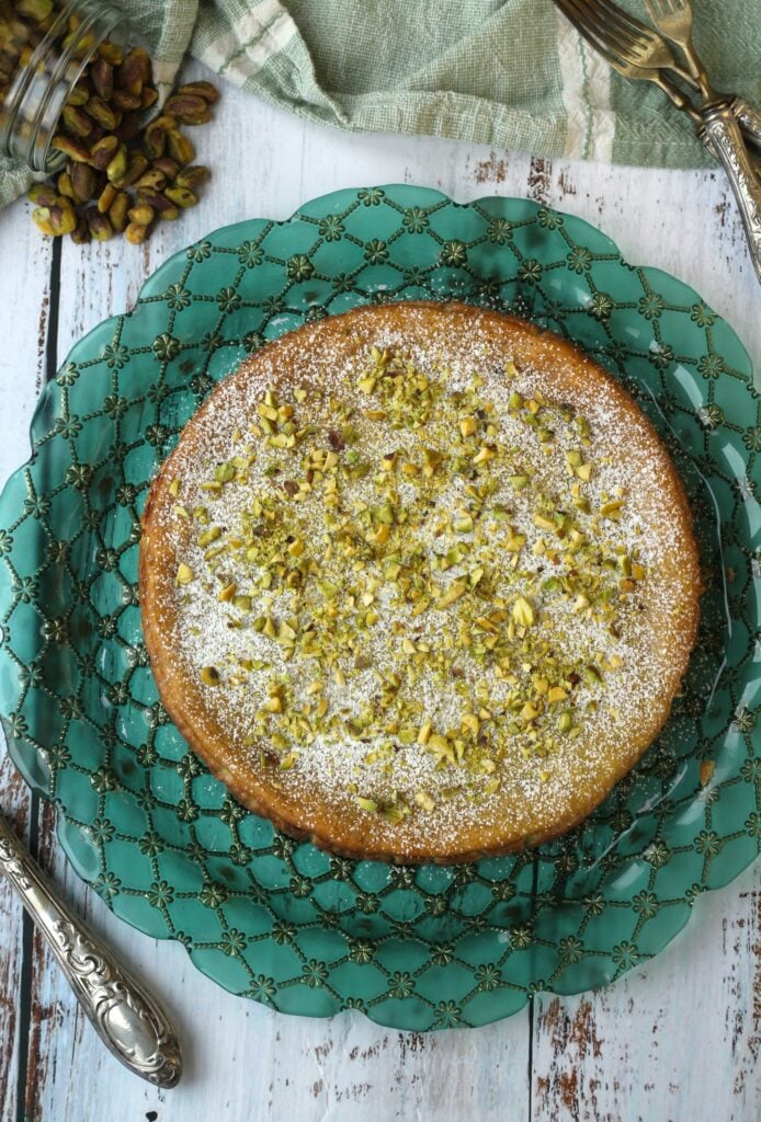 Ricotta pistachio cheesecake on green plate with pistachios on side.