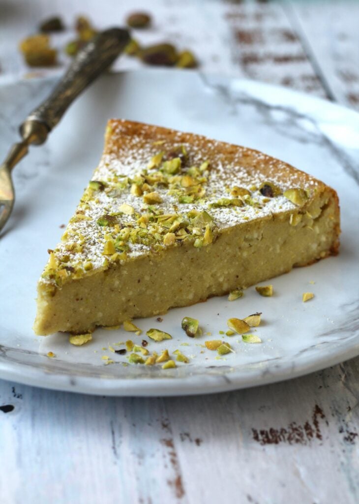 Wedge of no crust ricotta pistachio cheesecake with fork on plate.