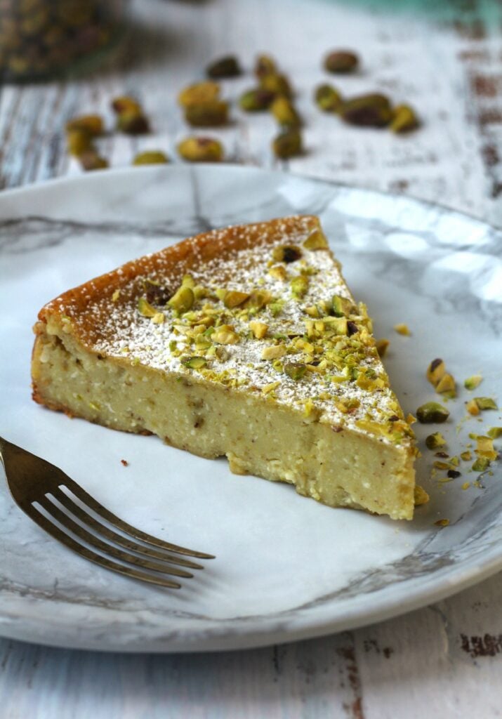 Slice of ricotta pistachio cheesecake on plate with fork.