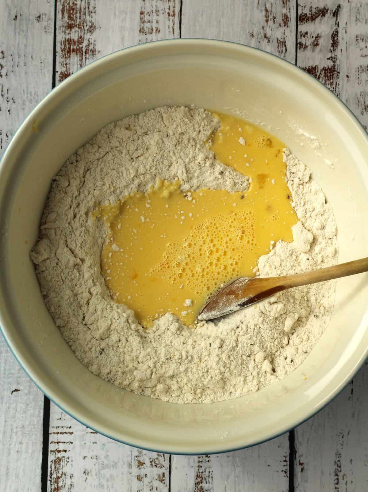 Eggs added to bowl with dry ingredients with wooden spoon.