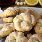 Sicilian lemon glazed anise taralli cookies piled on plate with coffee cup and halved lemon in background.