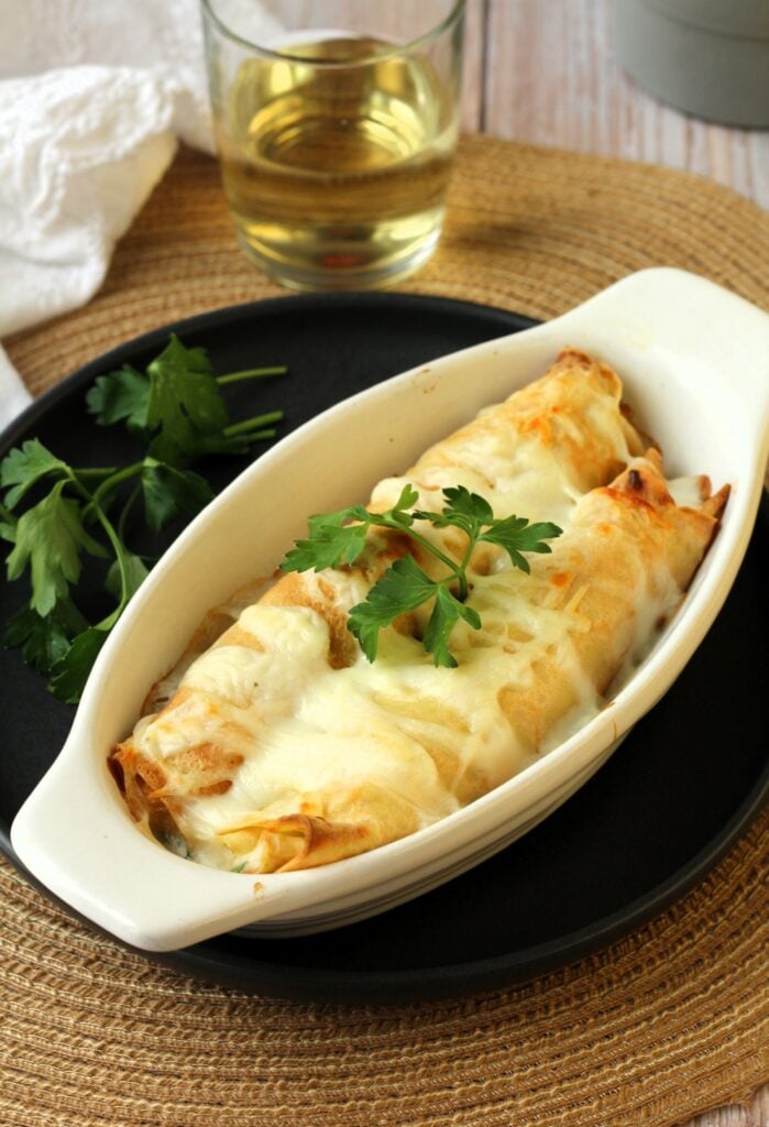 Seafood filled crepes with béchamel sauce in baking dish with parsley on top.