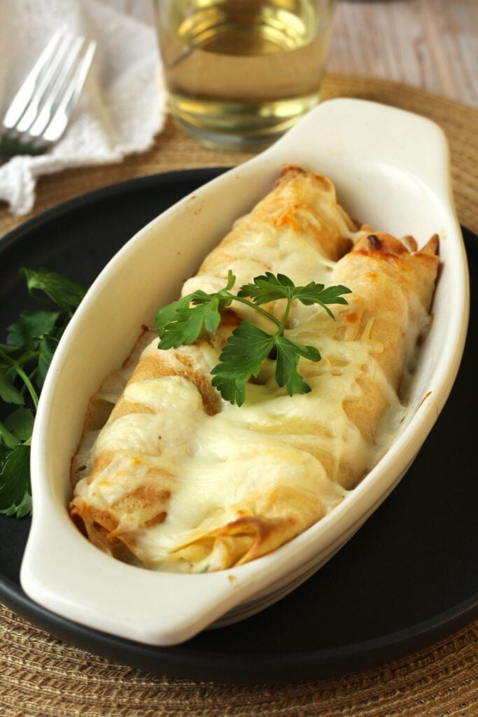 Seafood filled crepes topped with béchamel sauce in baking dish topped with parsley.