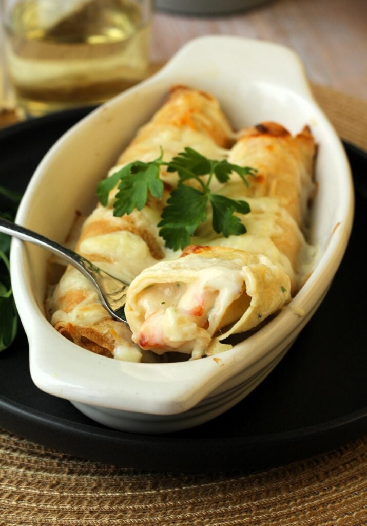 Forkful of shrimp and scallop seafood crepes in baking dish.