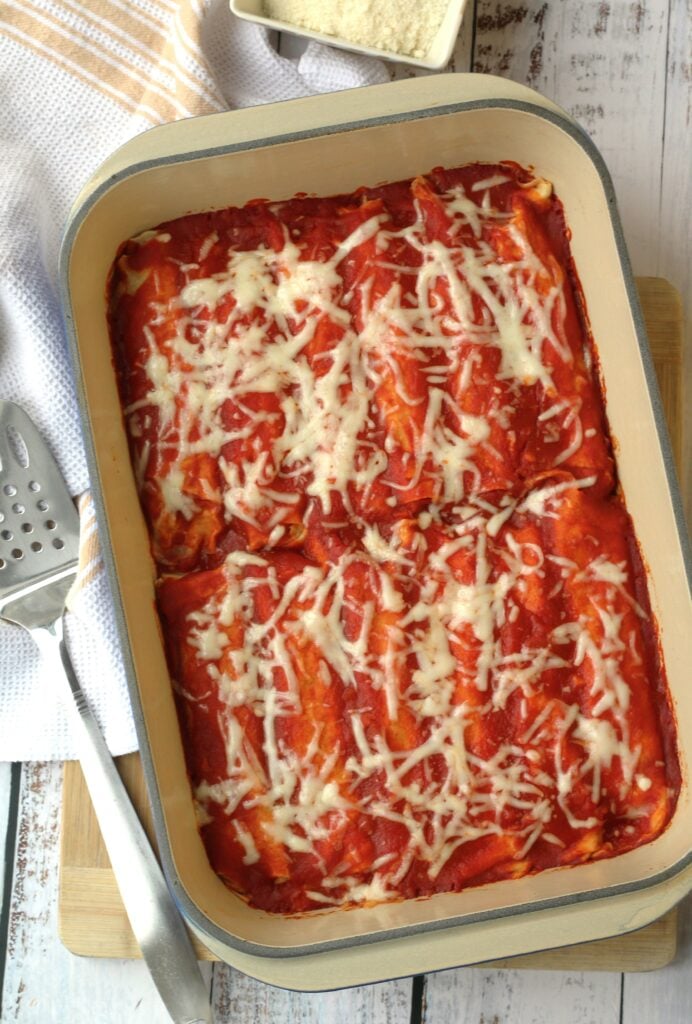 Italian crepes with meat filling topped with sauce and cheese in baking dish.