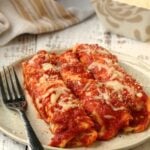 Crepes cannelloni with tomato sauce and cheese on plate with fork.