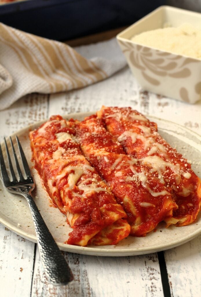 Crepes cannelloni with tomato sauce and cheese on plate with fork.