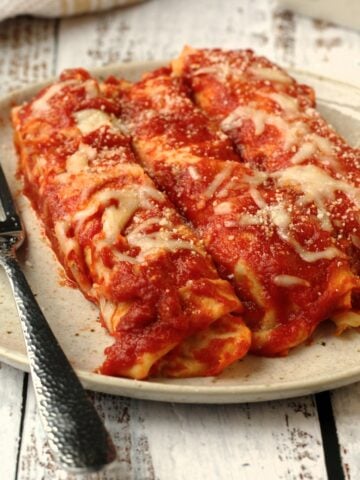 Italian crepes with meat filling topped with sauce on plate with fork.