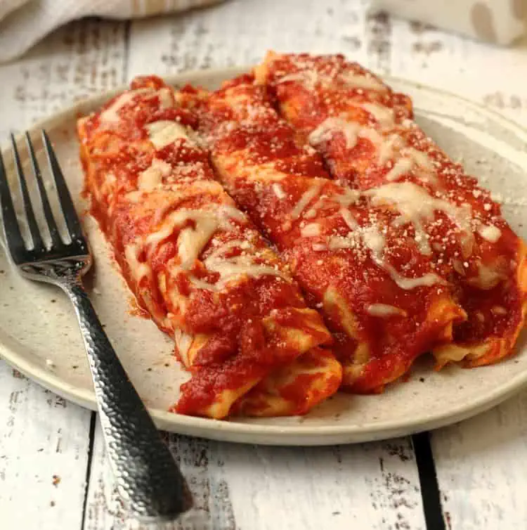 Italian crepes with meat filling topped with sauce on plate with fork.