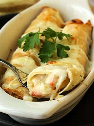 Seafood crepes in baking dish with fork cutting into them.