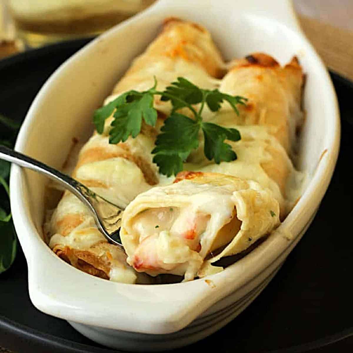 Seafood crepes in baking dish with fork cutting into them.