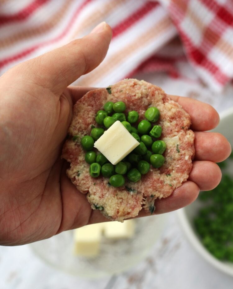 Mozzarella and peas filling in meatball mixture in palm of hand.