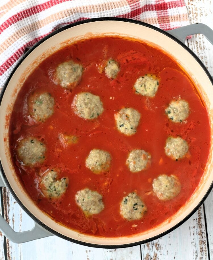 Meatballs simmering in tomato sauce in large skillet.