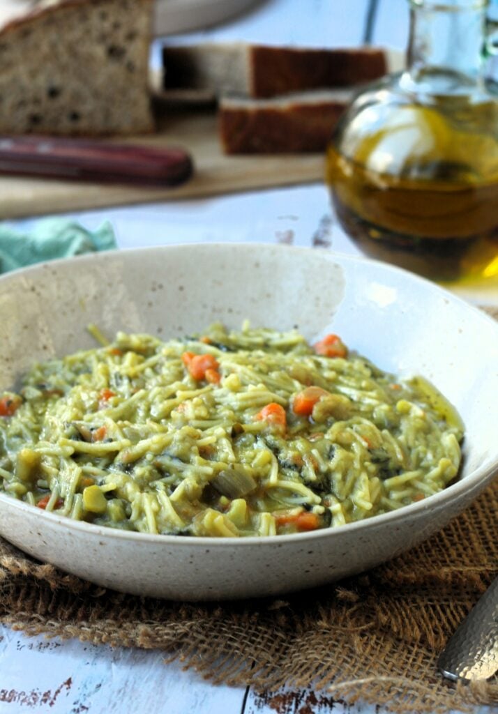 Bowl of fava bean soup with pasta in it with olive oil bottle and bread slices behind it.