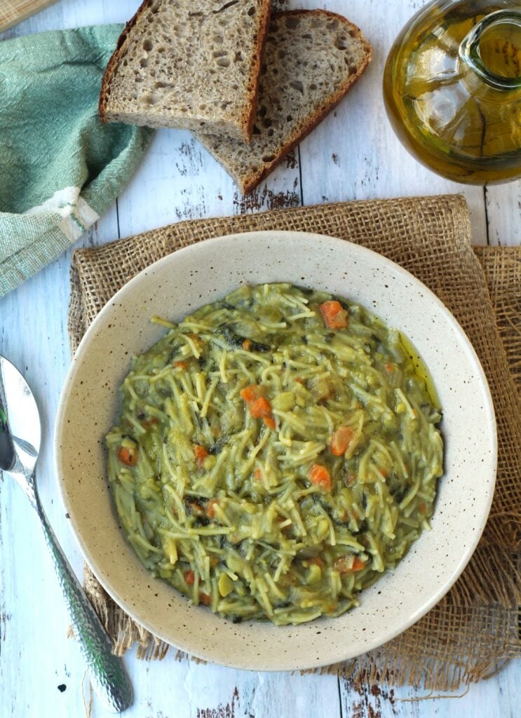 Bowl with fava bean soup with spoon, olive oil bottle and bread slices around it.