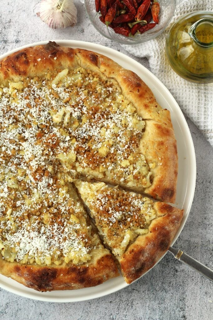 Overhead view of cauliflower pizza with spatula holding one slice.