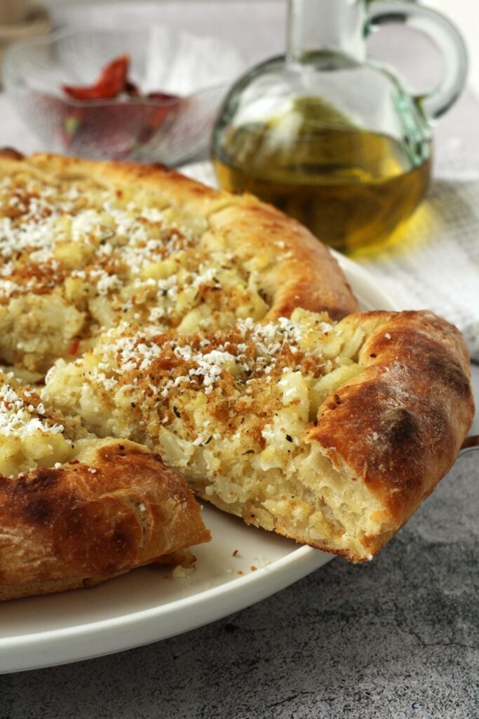 Wedge of pizza with cauliflower, breadcrumbs and ricotta salata on plate.