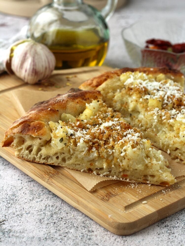 2 slices of pizza with cauliflower on wood board with olive oil botle and garlic bulb behind it.