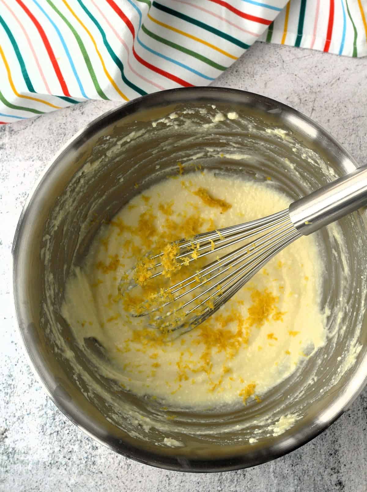 Lemon zest whisked into ricotta cookie batter in mixing bowl.