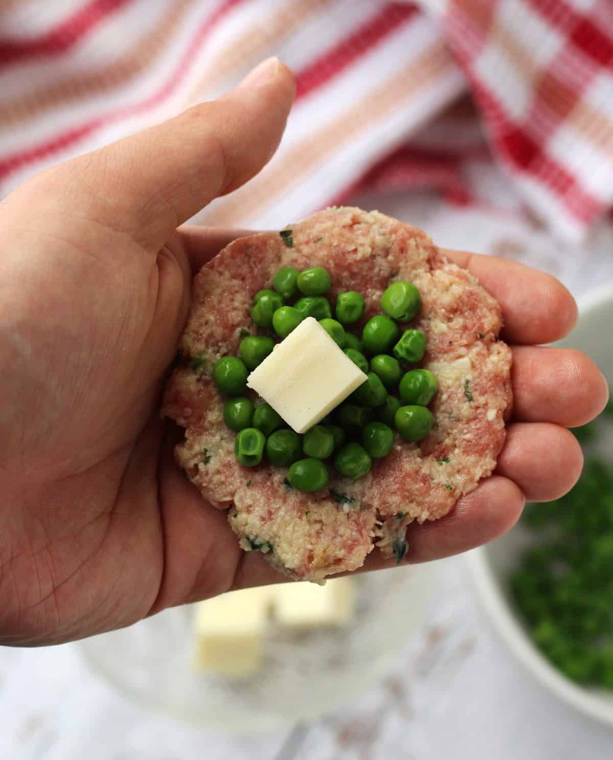 Palm hand containing peas and mozzarella square in center of meatballs.